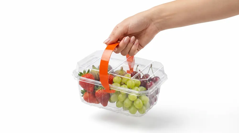 Hand carrying 1LB Vented Clamshell Pack with orange handle and mixed fresh fruit