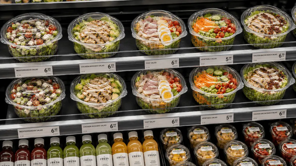 27oz clear PET salad bowls with hinged lids in refrigerated supermarket display