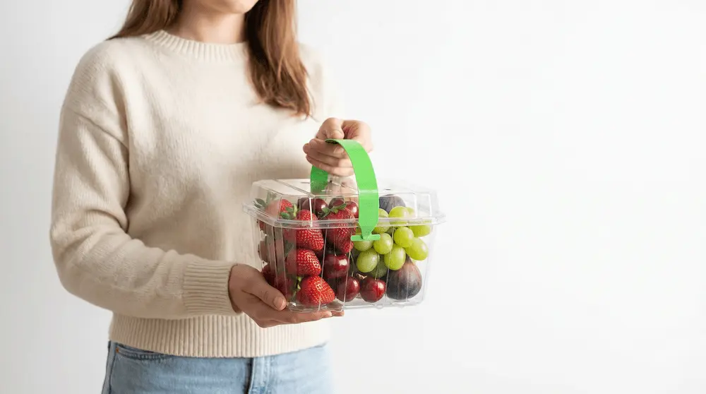 Person carrying 2LB Vented Berry Clamshell Container with green handle for portable fruit gift packaging