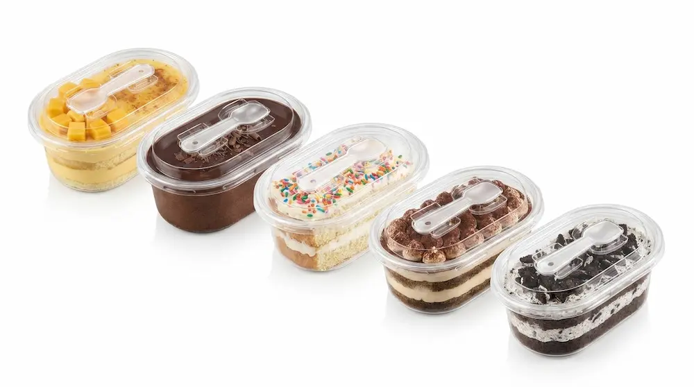 Assorted clear oval PET dessert containers with spoon lids for bakery display
