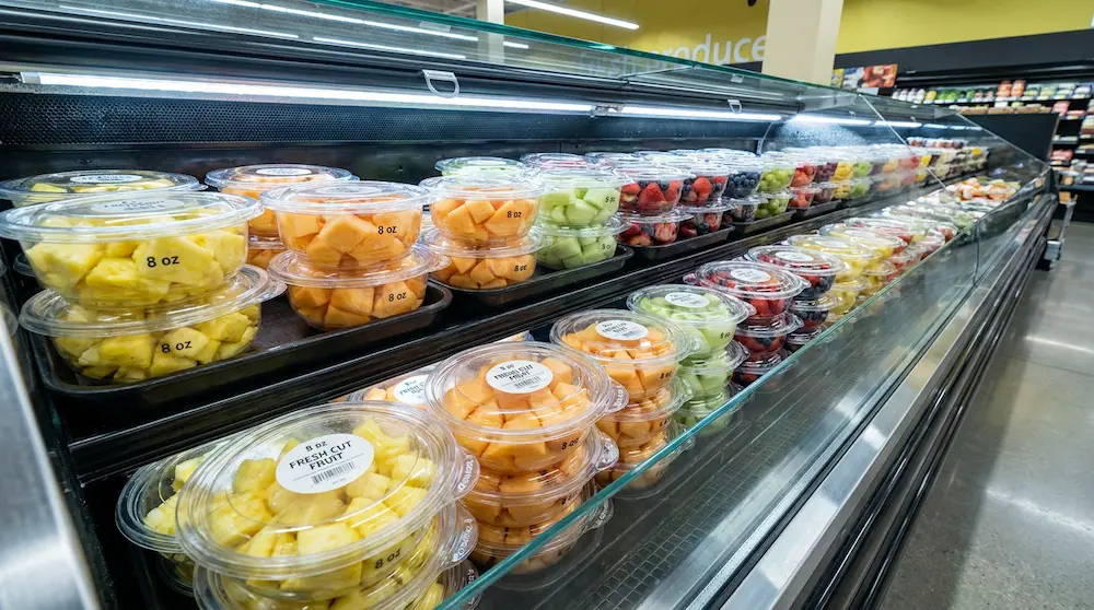 Clear rPET round bowls with tamper evident anti-fog dome lids for fresh-cut fruit island display in a premium supermarket