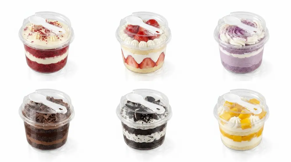 Six clear round PET dessert cups with integrated spoon lids for assorted desserts