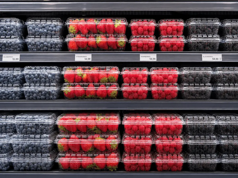 Clear PET Berry Containers FAQ: Materials, Sizes, Uses, and Ordering Questions 2 Clear PET berry containers displaying blueberries, strawberries, raspberries, and blackberries in a supermarket cooler
