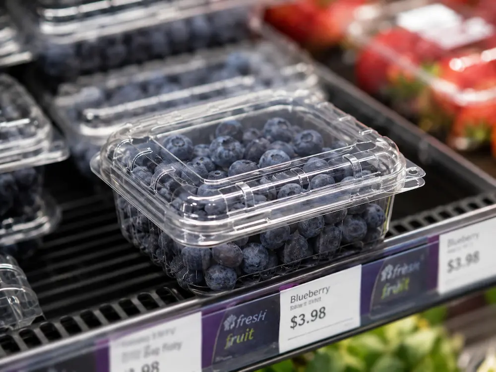 Clear PET blueberry clamshell tray displayed in a chilled supermarket produce case.