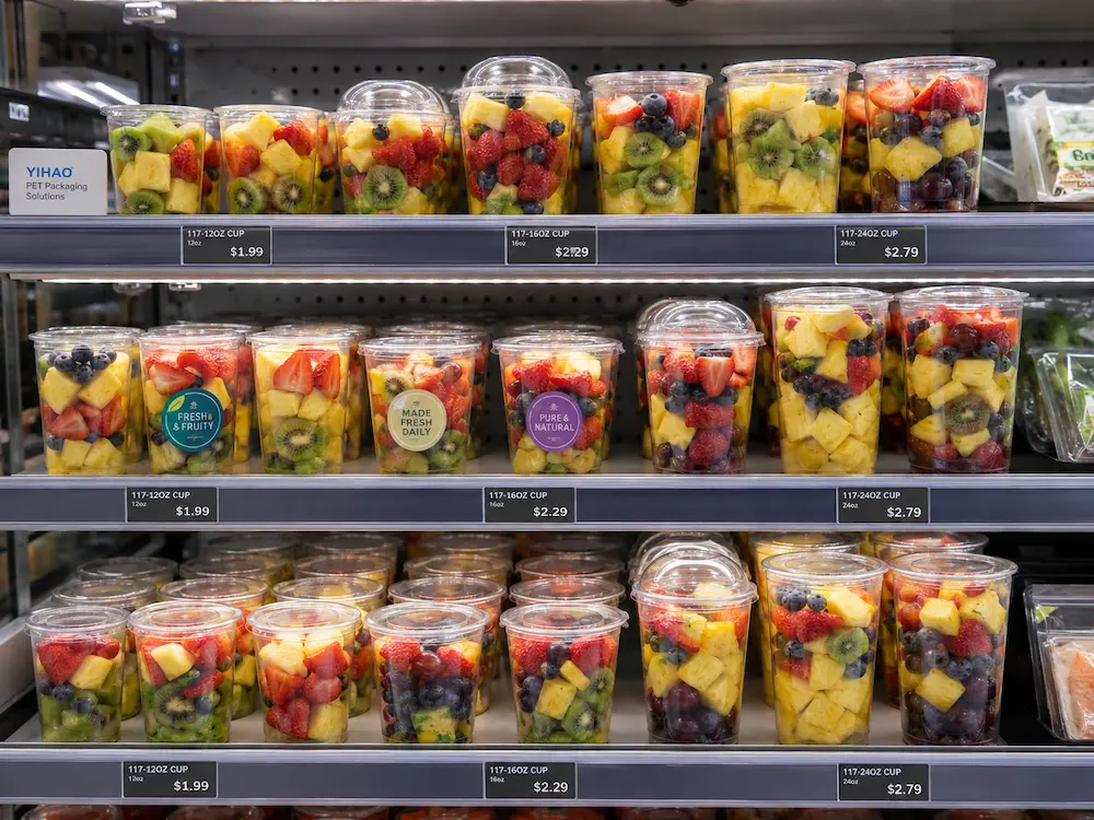 Clear PET fruit cups in refrigerated retail display for pineapple, berry mix, melon, and tropical fruit portions
