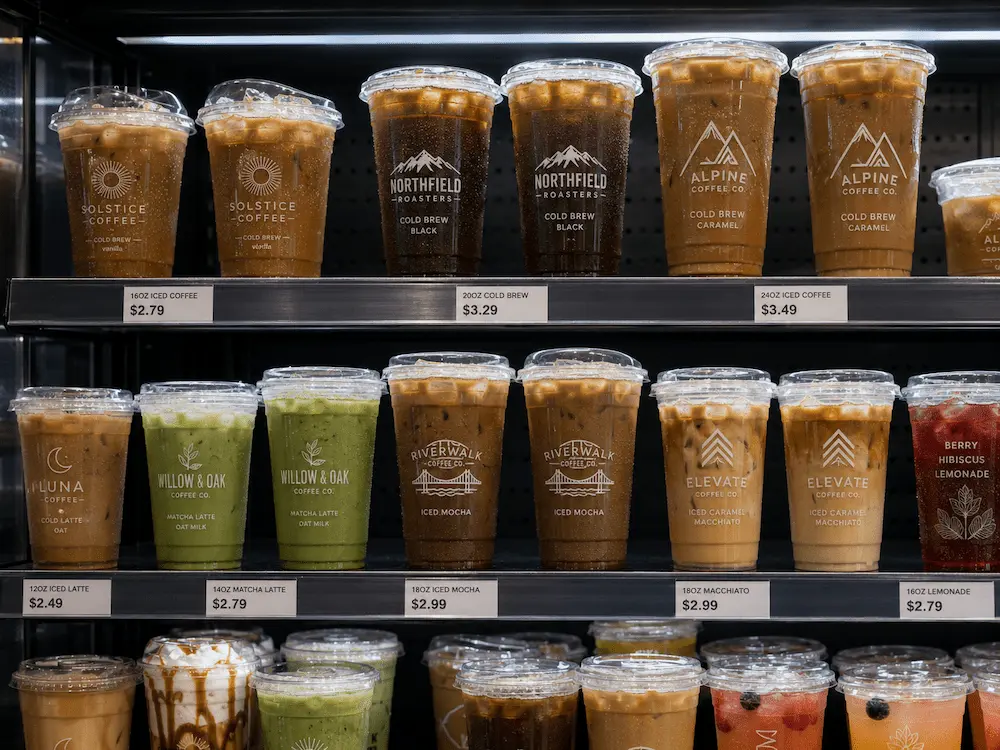 Supermarket refrigerated display with custom iced coffee cups, cold brew cups, and branded PET drink packaging.