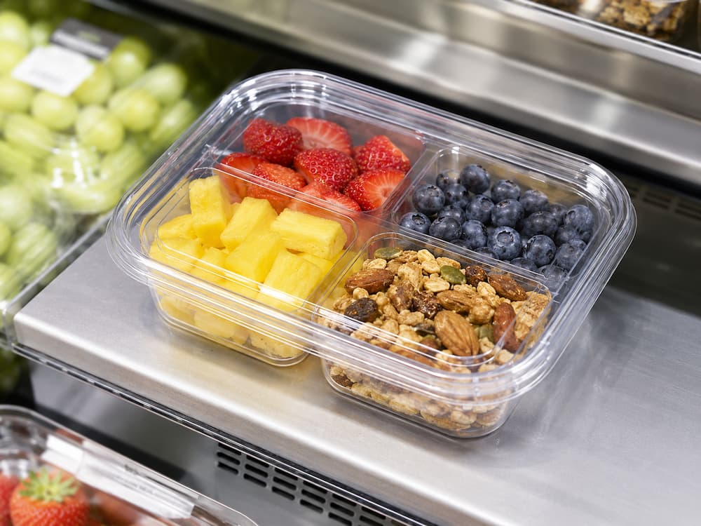 Four-compartment clear PET fruit salad container with pineapple, strawberries, blueberries, and granola.