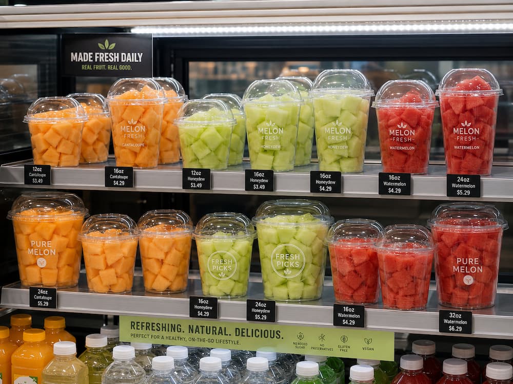 Fresh-cut melon containers in clear PET cups displayed in a chilled retail case with size and price labels.