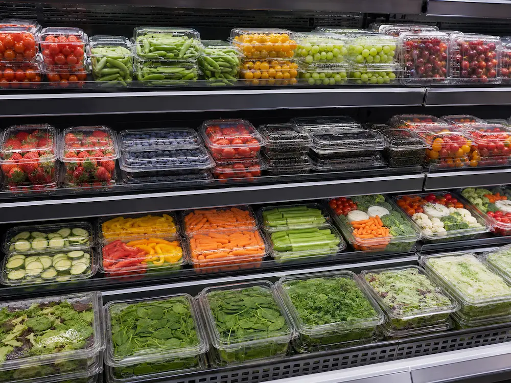 Supermarket Produce Trays FAQ: Materials, Sizes, Uses, and Ordering Questions 3 Supermarket produce trays displayed in a chilled case with vegetables, berries, tomatoes, grapes, and salads.