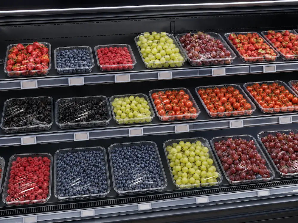 Supermarket produce trays displayed in refrigerated retail shelves