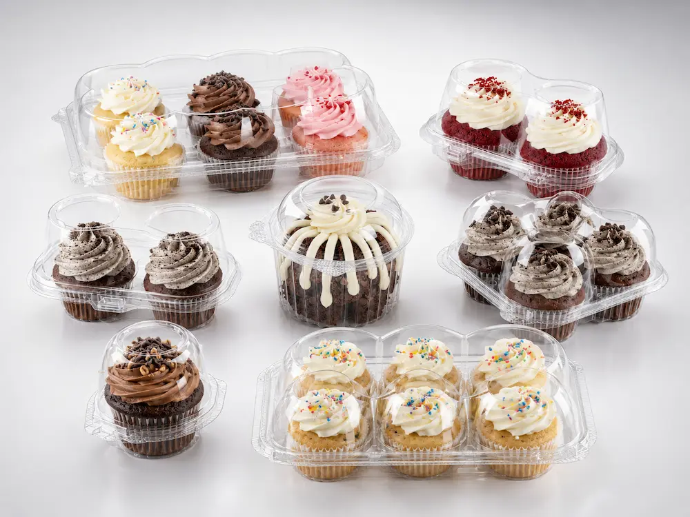 Clear PET cupcake containers and bakery packaging set with assorted cupcakes on a clean light gray studio background