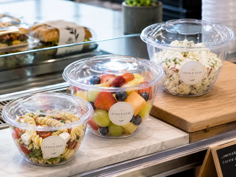 Deli Food Packaging FAQ: Materials, Sizes, Uses, and Ordering Questions 5 Clear PET deli containers filled with fruit, pasta salad and cold deli sides at a deli counter