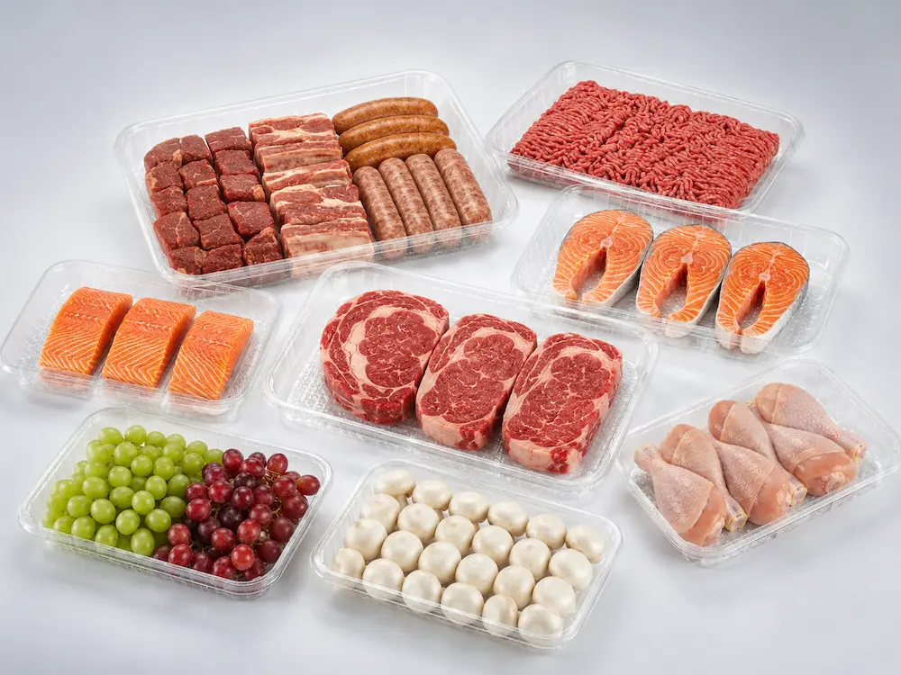 Clear PET fresh food trays with meat, seafood, grapes, and mushrooms in a premium cool gray studio composition