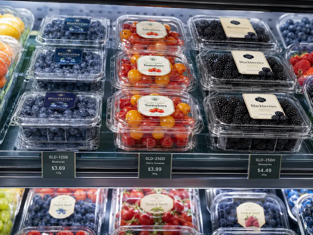 Clear PET fruit clamshell containers for blueberries, cherry tomatoes, and blackberries on a supermarket refrigerated shelf