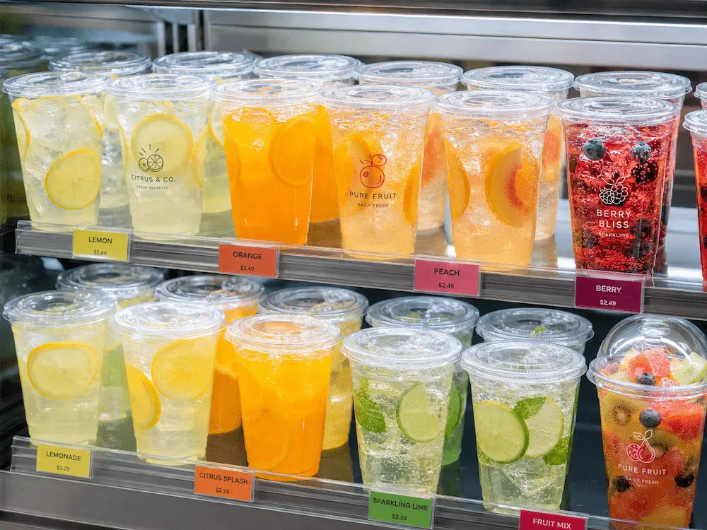 Clear PET juice cups with lemonade, orange drink, sparkling berry drink, and fruit beverages in a retail chiller display