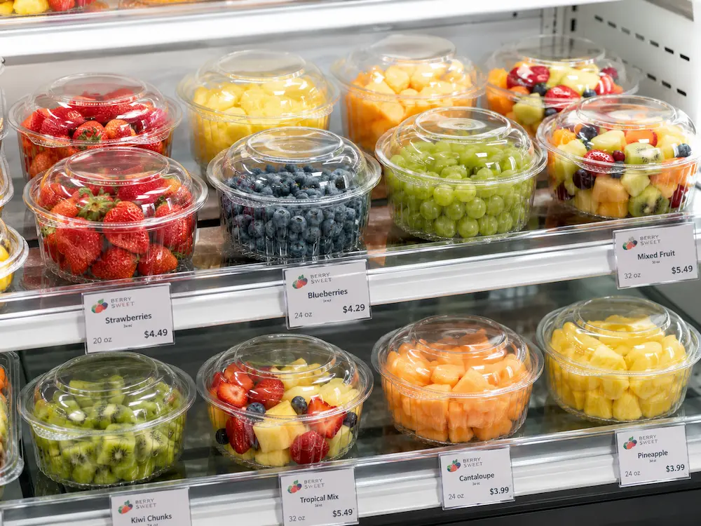 Clear PET farm packaging containers displayed with fresh fruit in a refrigerated retail case