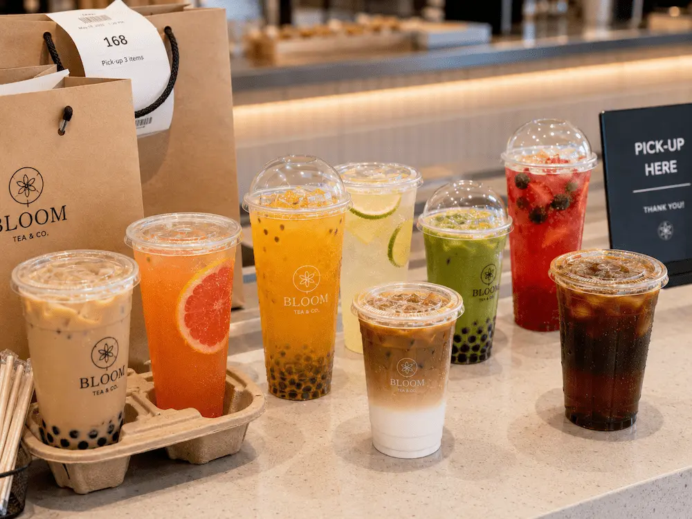 PET Bubble Tea Cups vs Alternative Packaging: How Buyers Should Choose 3 PET bubble tea cups with dome lids and flat lids on a takeaway pickup counter for milk tea, fruit tea, lemonade, matcha, and iced coffee