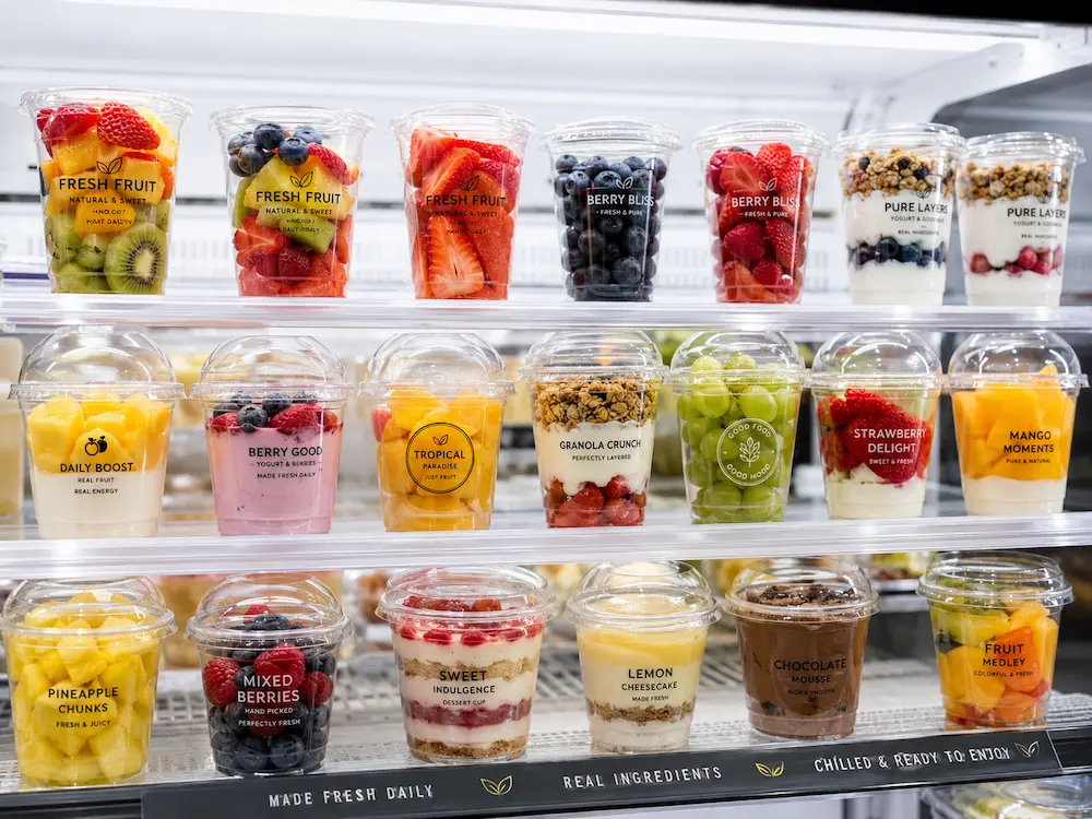 Printed PET cups displayed in a refrigerated retail shelf with fruit cups, yogurt desserts, and chilled grab-and-go food