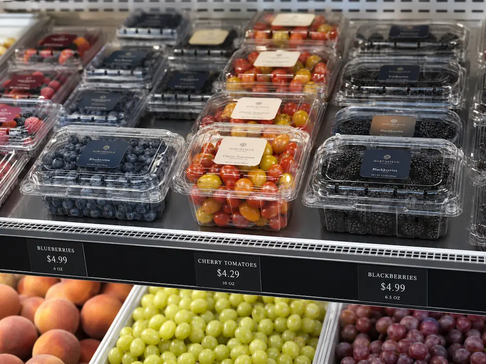 Refrigerated produce display with clear PET fruit clamshell containers for blueberries, cherry tomatoes, and blackberries