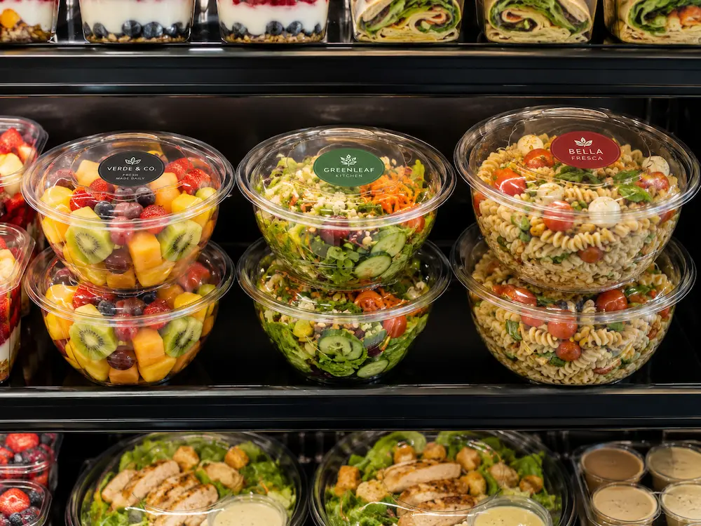 Round PET deli containers displayed in a refrigerated retail case with fruit salad and pasta salad