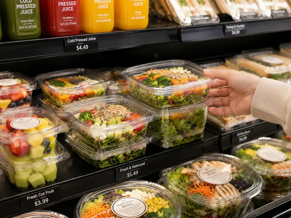 Shopper selecting a clear PET square salad container from a chilled grab-and-go display