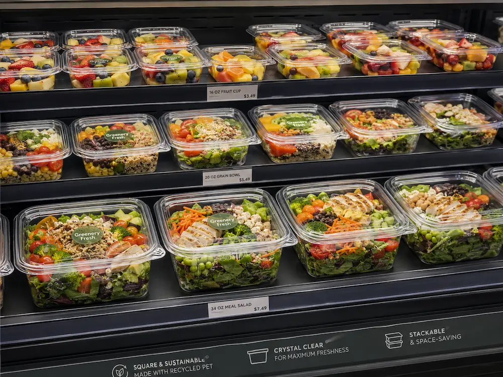 Grab-and-Go Square Packaging FAQ: Materials, Sizes, Uses, and Ordering Questions 2 Square PET grab-and-go containers displayed in a refrigerated case with fruit cups, grain bowls, and meal salads