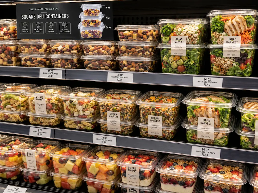Square PET deli containers displayed in a supermarket cold case for salads, fruit, and grab-and-go meals