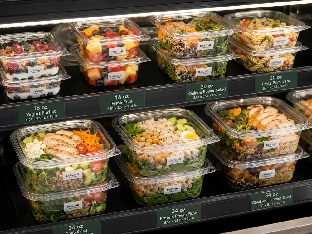 Grab-and-Go Square Packaging FAQ: Materials, Sizes, Uses, and Ordering Questions 5 Clear square salad containers stacked in a refrigerated retail shelf with fruit, pasta, quinoa, and chicken salad options