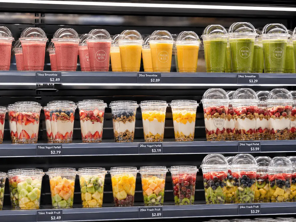 Clear smoothie cups displayed in a supermarket refrigerated shelf with fruit drinks