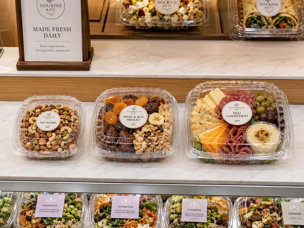 Best Nut Containers for Retail Display, Takeaway, and Chilled Food 7 Clear hinged nut containers displayed in a cafe takeaway counter with nuts, fruit, cheese, and deli snacks