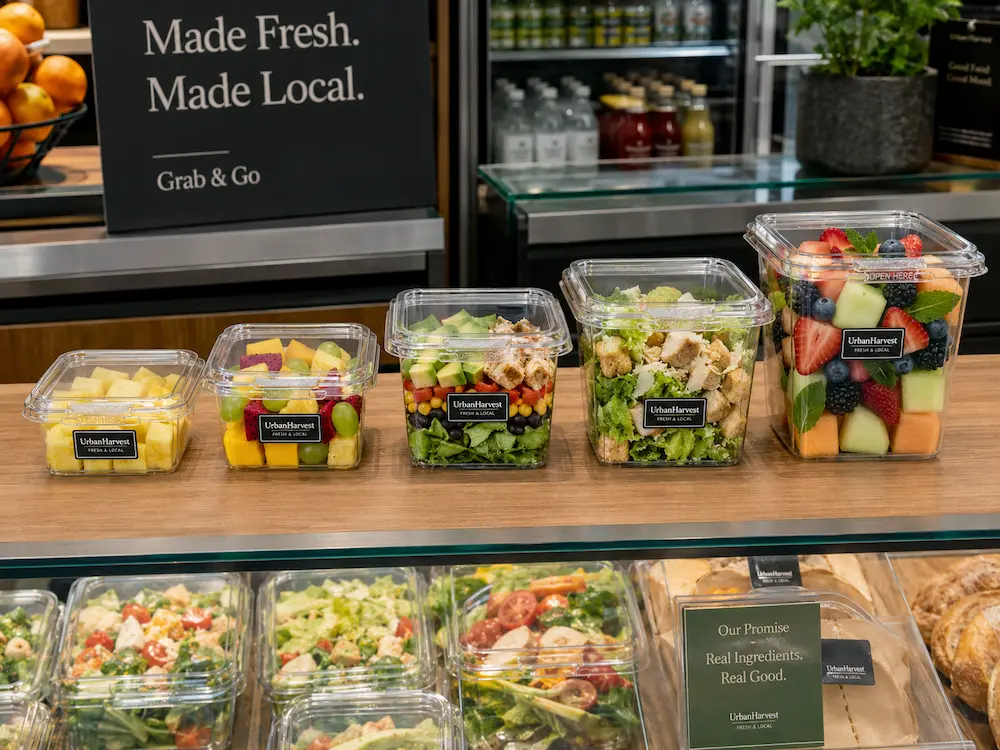 Clear tamper evident containers displayed in a grab-and-go retail food case with salads and fruit