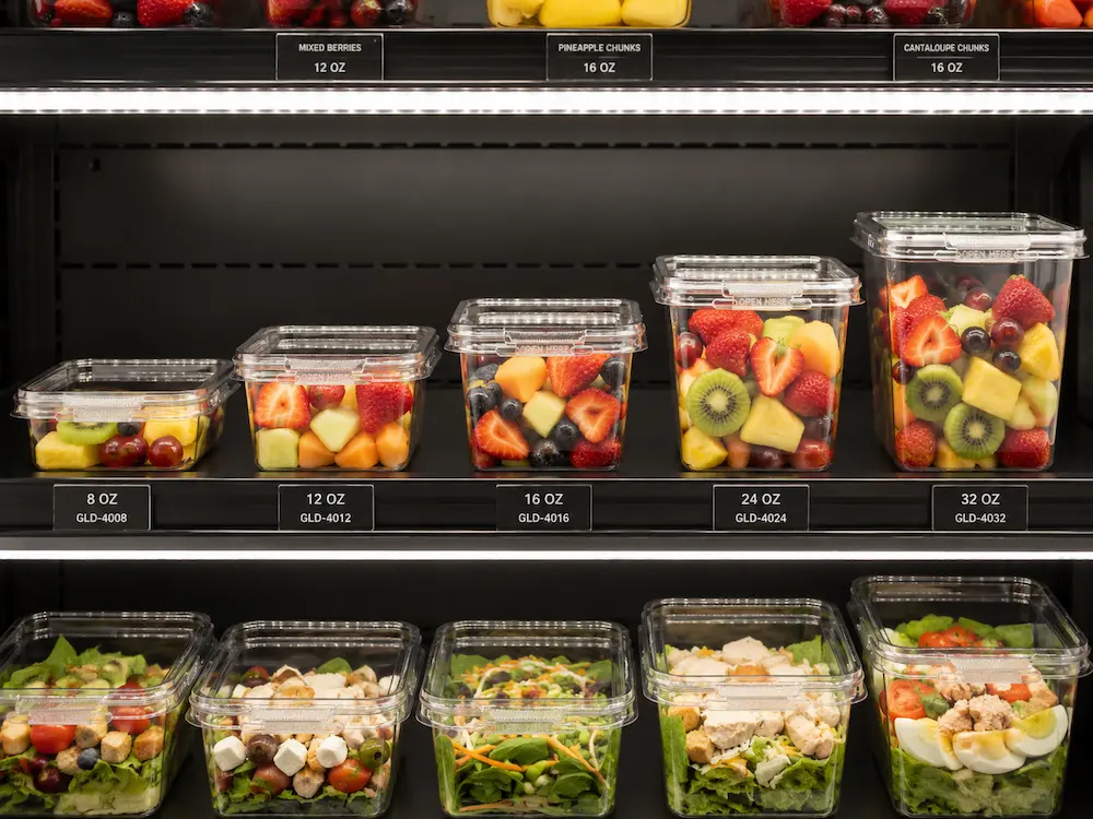 Clear PET tamper evident food containers displayed with fruit and salad in retail shelving